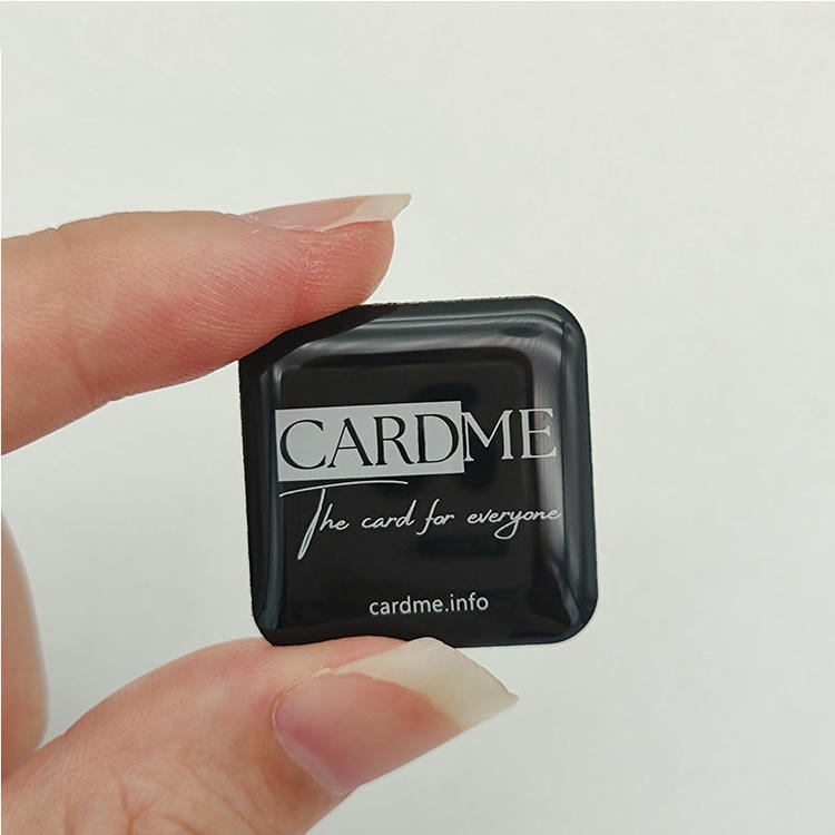 Hoge beveiliging NFC epoxy sticker getoond als een kleine vierkante koepel tag gehouden tussen vingers om compacte sabotage resistente labeling aan te tonen.