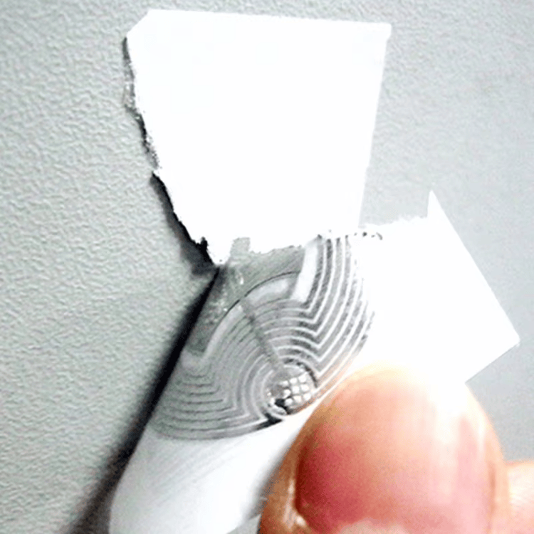 Deze afbeelding toont een close-up van een fragiel RFID-label dat wordt losgetrokken, waardoor de antennestructuur scheurt en onbruikbaar wordt.