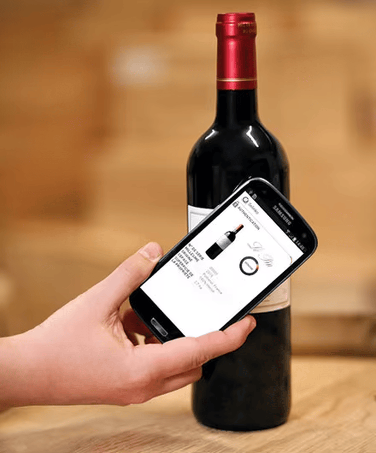 Deze afbeelding toont een mobiele telefoon die een tag op een wijnfles leest om digitale productinformatie en de authenticiteitsstatus weer te geven.