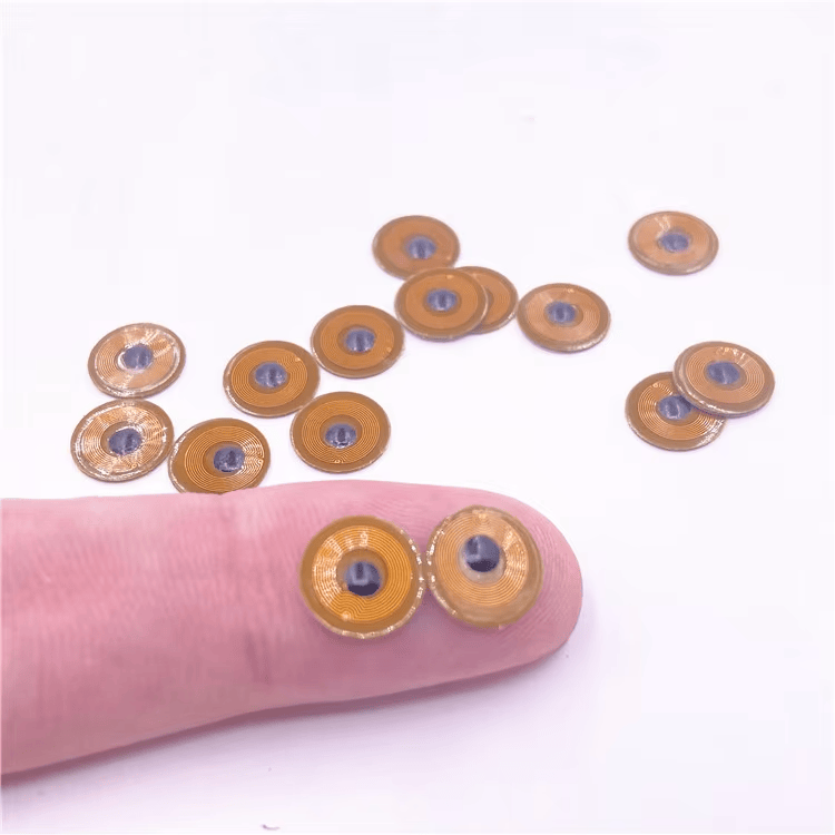 Twee FPC10-1 micro RFID-tags op een vingertop tonen het ultrakleine 10mm-formaat voor ingebouwde tracking op metaal.
