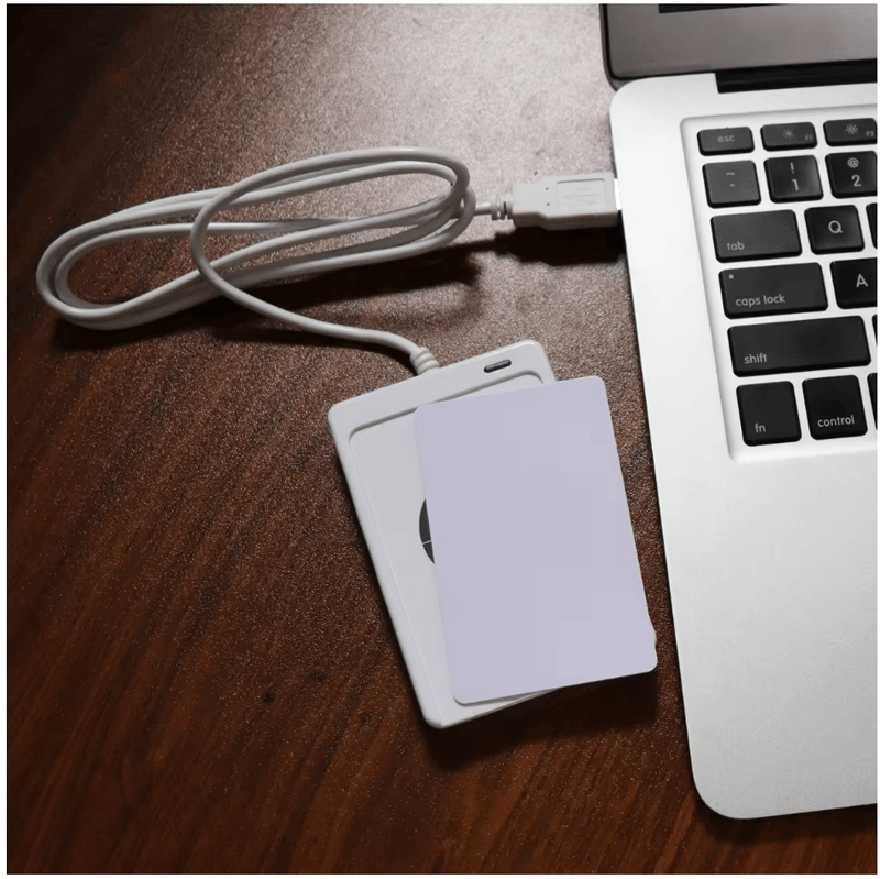 Deze afbeelding toont de ACR122U-lezer naast een laptop met een kaart op het leesoppervlak voor contactloze detectie.